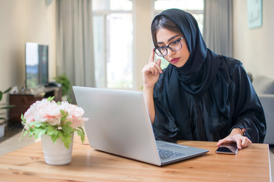 Pretty young middle eastern woman wearing hijab and eyeglasses using laptop at home
