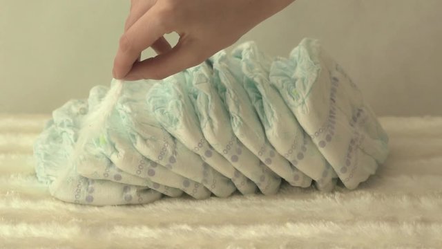 Mother holds a white gentle feather on baby diapers, the concept of comfort and lightness, slow motion