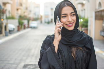 Portrait of a smiling young arabian woman talking on mobile phone on the city street