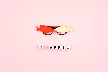 April Fools' Day celebration. Glasses with paper fish and text 1 April on pink background. All Fools' Day, humor, prank, joke concept