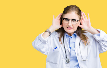 Middle age mature doctor woman wearing medical coat over isolated background Trying to hear both hands on ear gesture, curious for gossip. Hearing problem, deaf