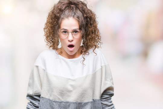 Beautiful brunette curly hair young girl wearing glasses over isolated background afraid and shocked with surprise expression, fear and excited face.