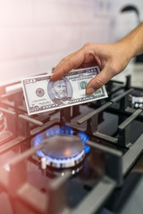 Cooktop with burning gas ring with hands holding money 50 dollars for combustion at home.