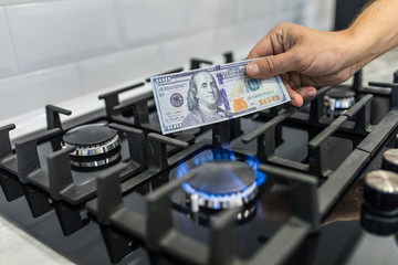 Cooktop with burning gas ring with hands holding money 100 dollars for combustion at home.
