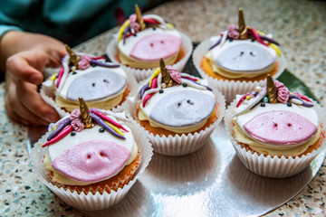 The child takes one of the festive cupcakes with a unicorn.