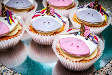 Festive cupcakes with a muzzle of a unicorn on a stand.