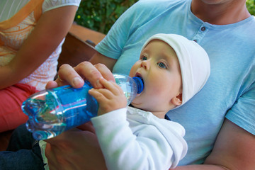 A small child sits and drinks water from a bottle.