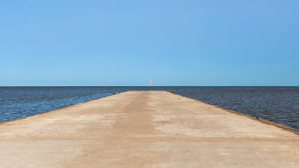Road leading to the sea to the horizon. Sailboat on the horizon.
