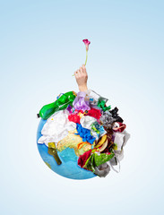 An earth globe covered with trash and male hand with a withering flower over white background, the...