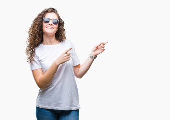 Beautiful brunette curly hair young girl wearing sunglasses over isolated background smiling and looking at the camera pointing with two hands and fingers to the side.