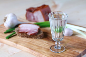 A glass of vodka is on a cutting board with a pieces of lard.