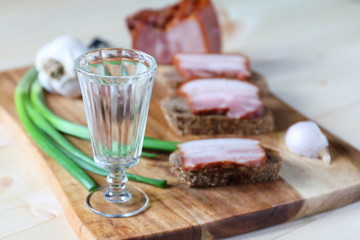 A glass of vodka is on a cutting board with a pieces of lard.