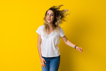 Beautiful young blonde woman jumping happy and excited over isolated yellow background