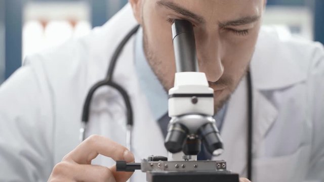 selective focus of male scientist looking through microscope in laboratory