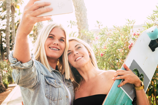 Happy coule of young caucasian attractive girls taking selfie picture with modern phone - braket for perfect teeth and youthful concept - people in summer outdoor leisure activity together