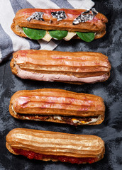 Different salty eclaires with cheese, ham, red caviar, spinach on a dark gray background