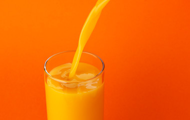 Orange juice pouring into glass, isolated on colour background, with copy space