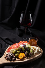 Prosciutto, ham, meat delicatessen chorizo on a cutting board with cheese, grapes, almond nuts, fig jam, glass of red wine on dark stylish background