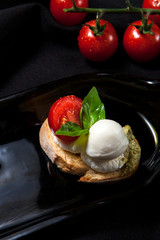 The author's presentation of bruschetta with cream cheese, mozzarella, cherry tomatoes and greenery on a dark stylish background
