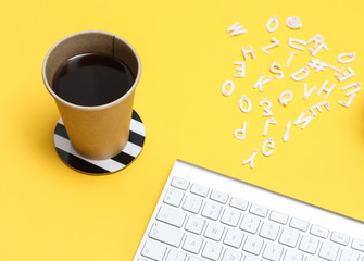 Relaxed office desk with a cup of coffee and a keyboard  on yellow background.