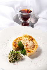 Quiche with chicken, tomatoes and greens on a white background whit a cup of tea