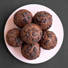 Chocolate muffins on pink plate on black table, top view. Flat lay, from above.