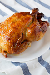 Homemade traditional rotisserie chicken on white plate, low angle view. Closeup.