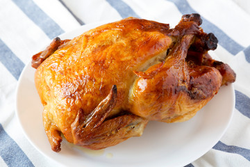 Homemade tasty rotisserie chicken on white plate, side view. Close-up.