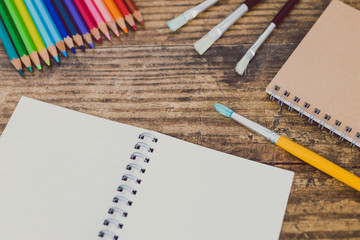 Obraz premium notebook with brushes and color pencils on wooden desk