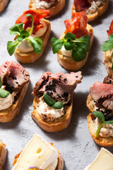 Different types of bruschetta with meat and cheese on a gray concrete background close-up