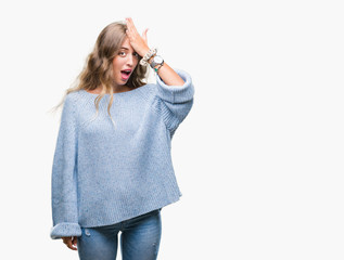 Beautiful young blonde woman wearing winter sweater over isolated background surprised with hand on...