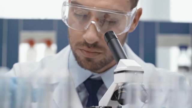 male scientist in goggles looking through microscope in laboratory