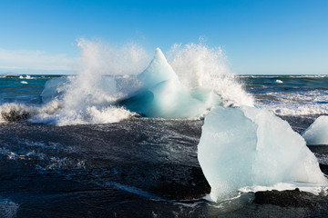 Surf crashing into ice chunks washed on Diamond Beach near glacier lagoon of Jokulsarlon, Iceland,...