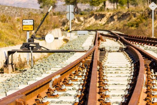 A railroad switch track with traffic signs, mountains and trees in the background