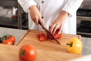 Photo of european woman chef wearing white uniform making salad with fresh tomatoes, in kitchen at the restaurant