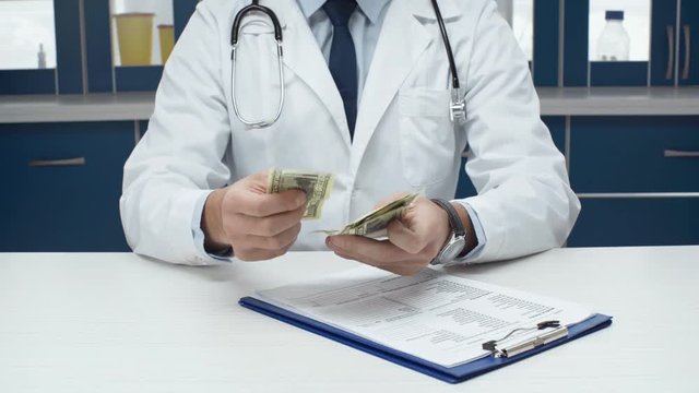 cropped view of male doctor in white coat sitting at table with diagnosis, counting and putting money in pocket