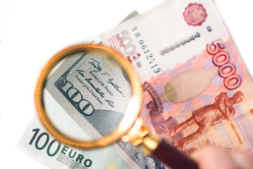 Hundred dollar under a magnifying glass on the bacdrop euro and ruble banknotes. Сoncept of the main international currency