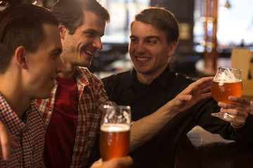 Company having fun and hanging out in bar. Friends laughing, holding beer glasses, looking away. Men communicating and resting at weekends in beer house or brewery together.