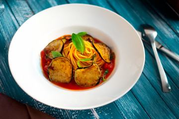 Vegetarian Spaghetti pasta with eggplants and tomato sauce on a white plate and wooden blue background