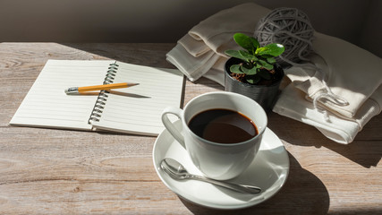 coffee cup, pencil and notebook on wooden in the morning light.