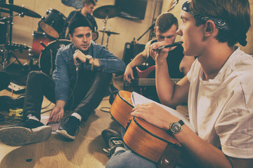 Members of rock band composing songs and training on repetition in studio. Handsome boy in bandana...