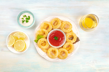 A plate of squid rings, shot from the top with lemon slices, two dips, a glass of wine, and a place for text