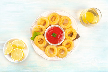 A plate of squid rings, shot from above with lemon slices, a dip, a glass of wine, and copy space