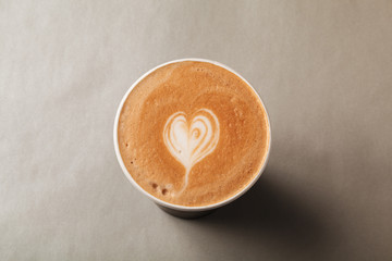 Paper cup of latte or cappuccino with patterned heart latte art on a grey background. Coffee to take away, coffee to go