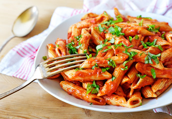 Delicious pasta dish with fresh basil on a wooden table. Top view scene, healthy eating or healthy lifestyle. Penne napoli or pasta arrabiata, closeup shot.