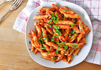 Delicious pasta dish with fresh basil on a wooden table. Top view scene, healthy eating or healthy lifestyle. Penne napoli or pasta arrabiata, closeup shot.