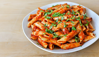 Delicious pasta dish with fresh basil on a wooden table. Top view scene, healthy eating or healthy lifestyle. Penne napoli or pasta arrabiata, closeup shot.