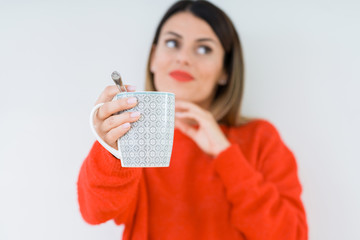 Young woman drinking cup of coffee over isolated background serious face thinking about question,...