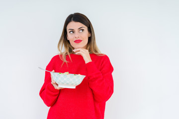 Young woman eating fresh healthy salad over isolated background serious face thinking about question, very confused idea