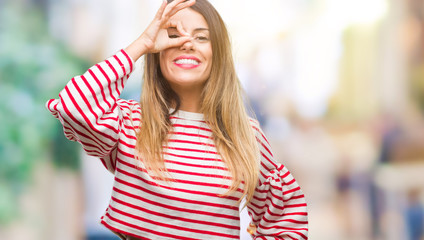 Young beautiful woman casual stripes winter sweater over isolated background doing ok gesture with hand smiling, eye looking through fingers with happy face.